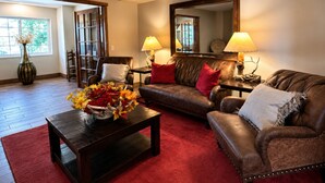 A living room with a brown leather sofa, a wooden coffee table, and a red rug. There is a large mirror on the wall and a vase with flowers on the coffee table. - Microtel Inn & Suites by Wyndham Bozeman (Bozeman)
