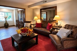 A living room with a brown leather sofa, a wooden coffee table, and a red rug. There is a large mirror on the wall and a vase with flowers on the coffee table. - Microtel Inn & Suites by Wyndham Bozeman (Bozeman)