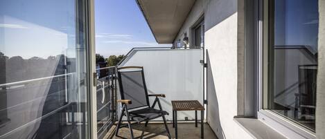 A balcony with a chair and a small table, a glass door, and a window.