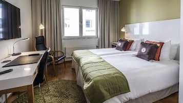 A hotel room with a bed, a desk, a chair, a TV, and a window with curtains.