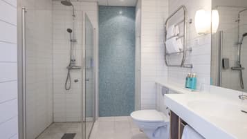 Un baño moderno con ducha de vidrio, inodoro blanco y lavamanos con espejo.