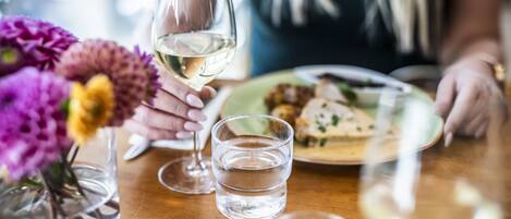 Una mesa de comedor con una copa de vino blanco, un vaso de agua y un plato de comida.