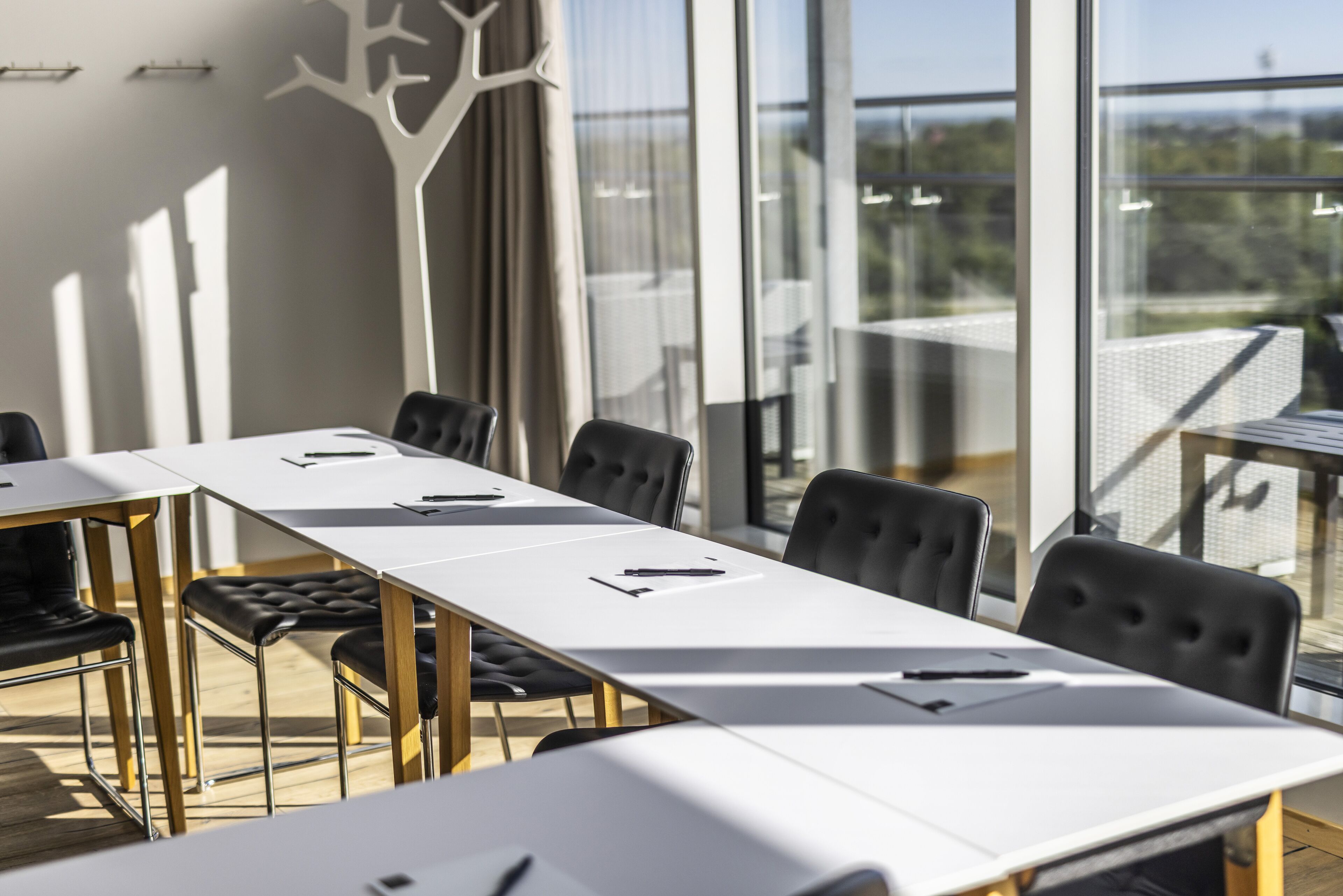 Uma sala de conferências com uma mesa comprida, cadeiras pretas e vista para o exterior através de grandes janelas.