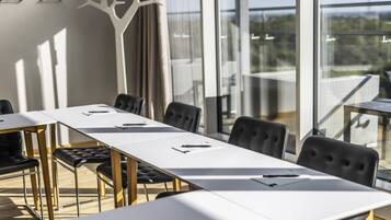 Uma sala de conferências com uma mesa comprida, cadeiras pretas e vista para o exterior através de grandes janelas.