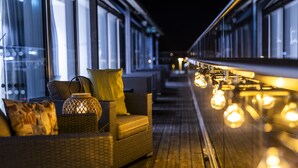 Una terraza de madera con mobiliario de mimbre e iluminación colgante.