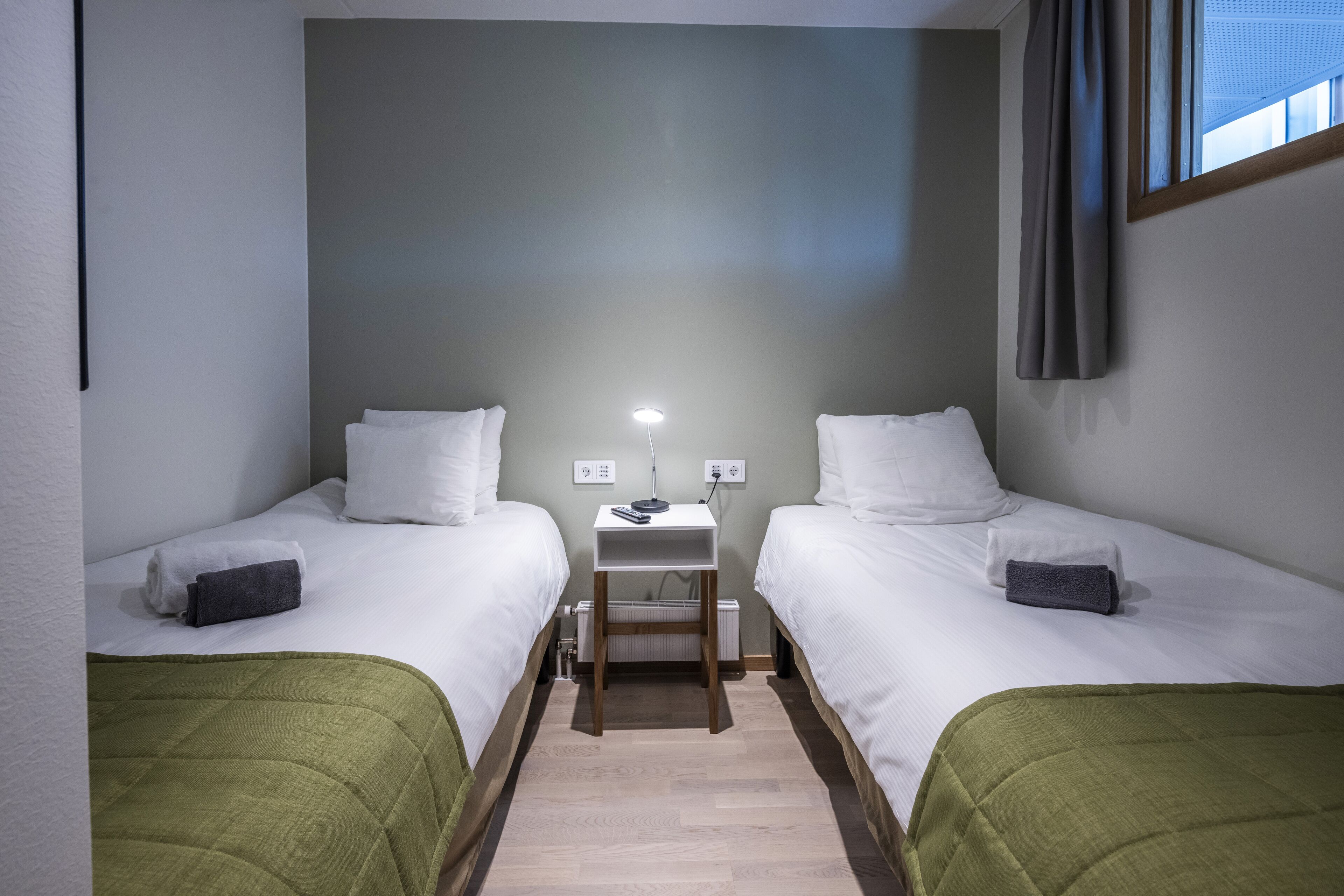 A twin room with two beds, a nightstand, and a lamp.