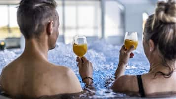 Two people in a hot tub holding glasses of orange juice.
