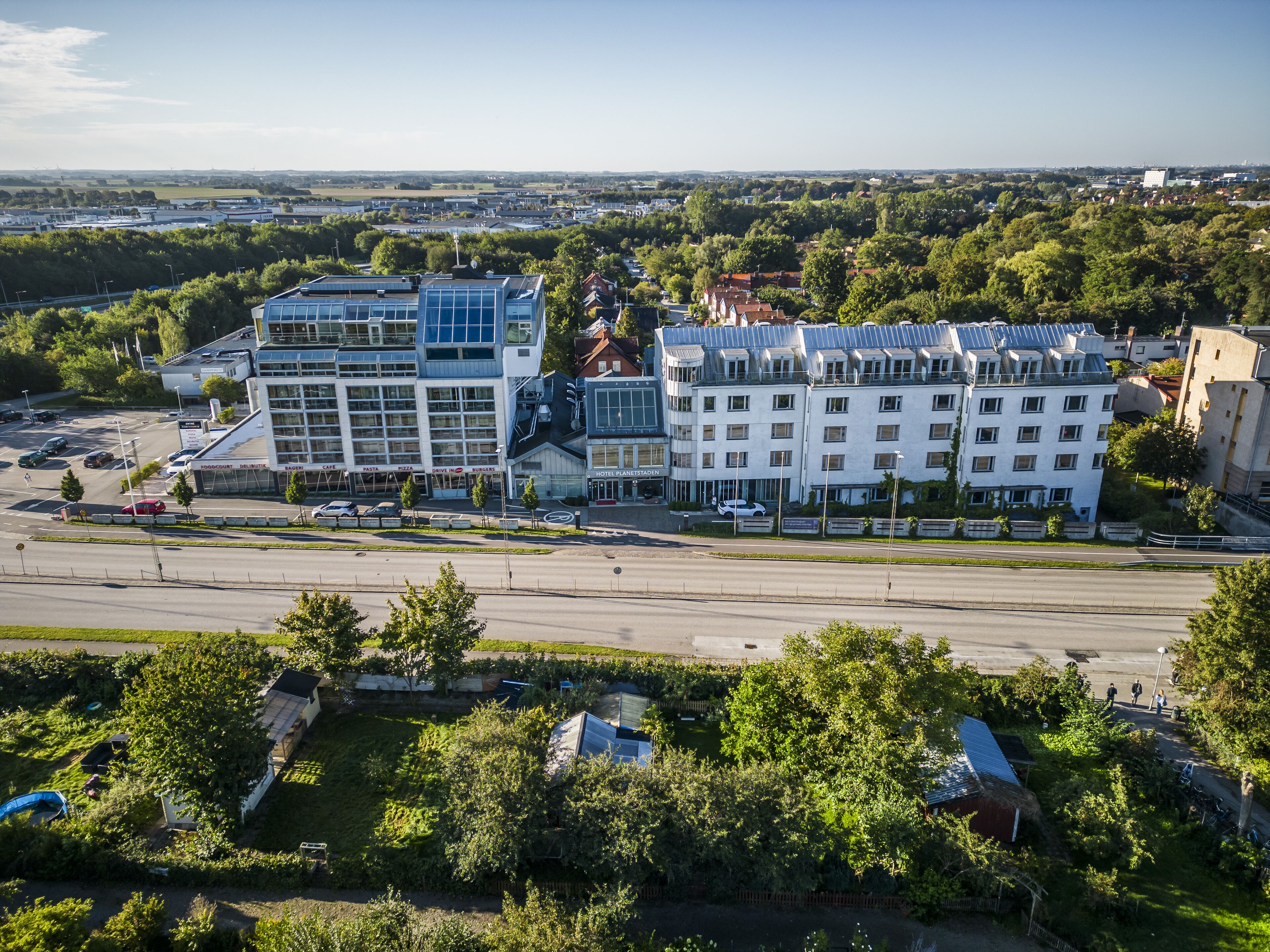 A modern hotel with multiple floors, large windows, and a parking lot in front.