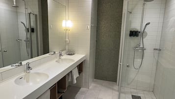 A modern bathroom with two sinks, a large mirror, a shower with a glass door, and a tiled floor.