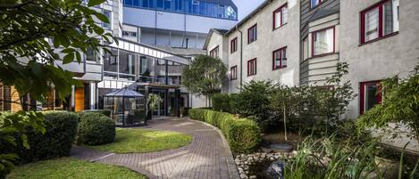 Een binnenplaats met een pad van bakstenen, een klein waterpartij en strakke hagen.