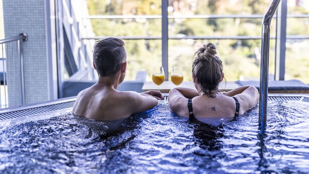 Dos personas en un jacuzzi con vistas a zonas verdes.