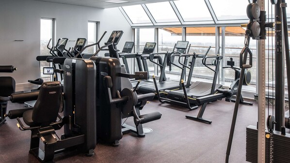 A gym with various exercise machines, large windows, and a view of the city.