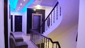 A hallway with a staircase, a door, and two upholstered chairs. - Hotel Surya International (New Delhi)
