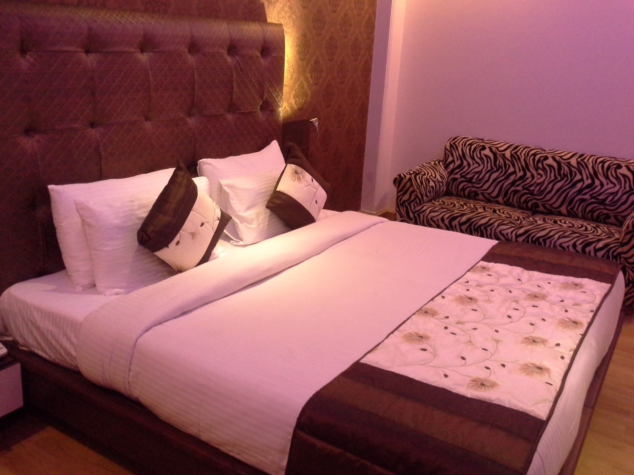 A neatly made bed with a headboard, pillows, and a blanket. There is a zebra-patterned sofa in the room.