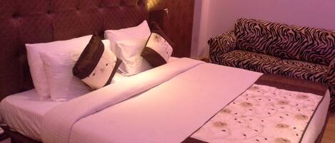 A neatly made bed with a headboard, pillows, and a blanket. There is a zebra-patterned sofa in the room.