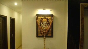 A hallway with a framed religious painting on the wall, a small table with a lamp, and a door on the left. - Hotel Surya International (New Delhi)