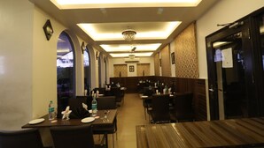 A restaurant with a long counter, multiple tables, and a chandelier. - Hotel Surya International (New Delhi)