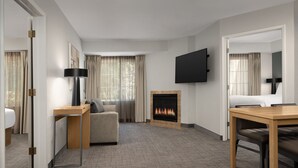 A modern hotel room with a fireplace, a flat-screen TV mounted on the wall, a sofa, a dining table, and a carpeted floor. - Residence Inn Marriott Palo Alto Los Altos (Los Altos)