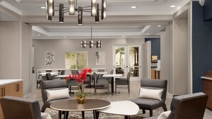 A modern dining area with a round table, grey upholstered chairs, and a vase of red flowers. - Residence Inn Marriott Palo Alto Los Altos (Los Altos)