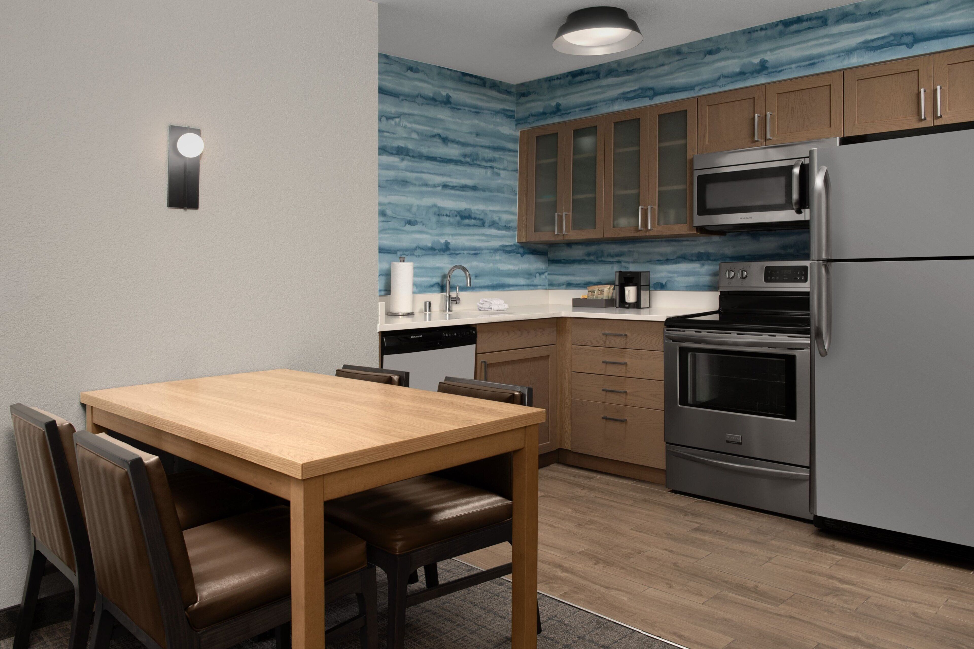 A modern kitchen with wooden cabinets, stainless steel appliances, and a wooden dining table with chairs.
