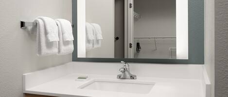 Un baño con un lavamanos blanco, un espejo y dos toallas colgadas en un perchero.