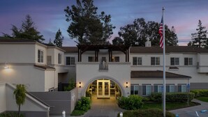 A multi-story building with a central entrance, a flagpole, and a landscaped garden area. - Residence Inn Marriott Palo Alto Los Altos (Los Altos)