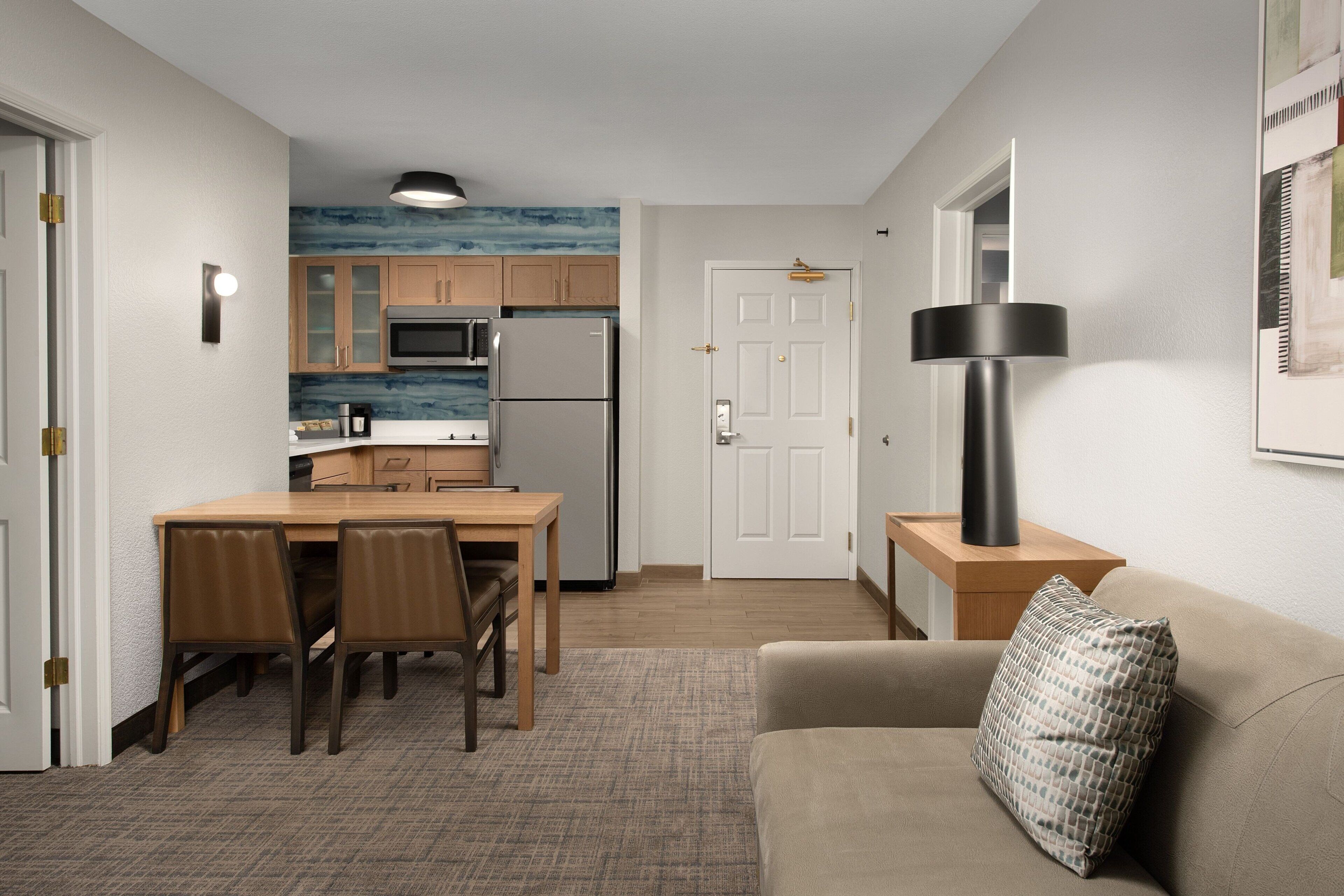 Un espacio habitable compacto con kitchenette, comedor y zona de estar con lámpara y cojín.