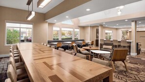 A spacious meeting room with a long wooden table, comfortable seating, and large windows offering views of the outdoors. - Residence Inn by Marriott San Jose South\/Morgan Hill (Morgan Hill)