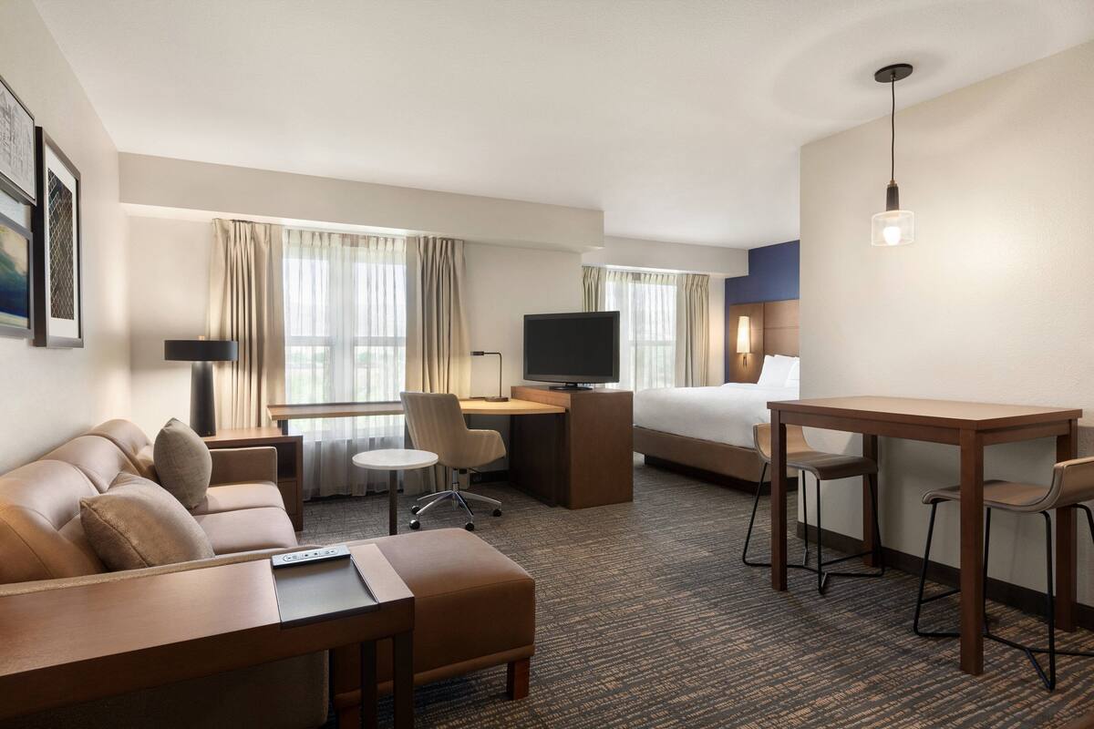 A hotel room with a sofa, a desk, a TV, a bed, and a dining table.