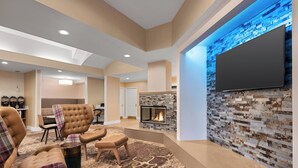 A modern living room with a fireplace, comfortable seating, and a flat-screen TV mounted on a textured wall. - Residence Inn by Marriott San Jose South\/Morgan Hill (Morgan Hill)