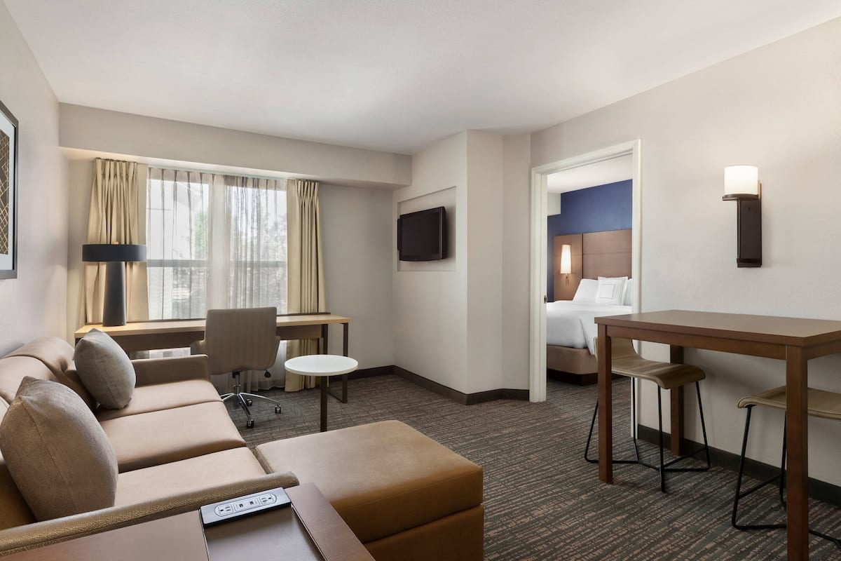 A hotel room with a sofa, a desk, a chair, a small table, a TV, and a bed.