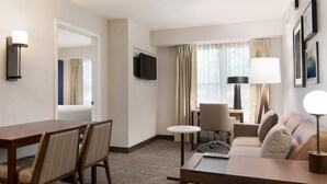 A hotel room with a dining table, chairs, a sofa, a TV, and a lamp. - Residence Inn by Marriott San Jose South\/Morgan Hill (Morgan Hill)