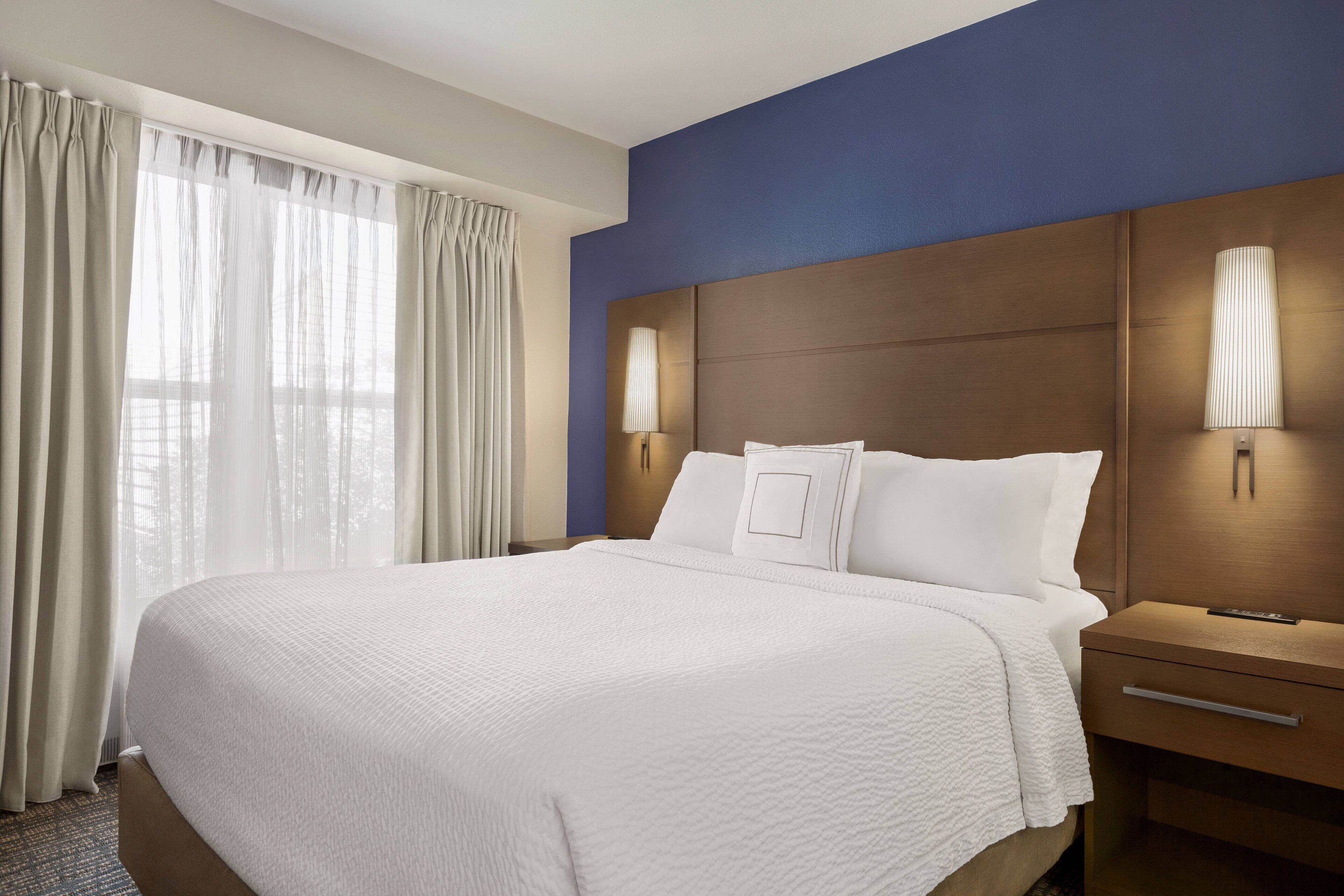 Een hotelkamer met een groot bed, twee nachtkastjes en een raam met gordijnen.