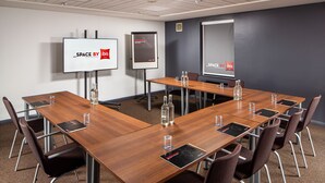 Una sala de conferencias con una mesa larga, sillas, una pantalla de proyector y una pantalla de presentación.
