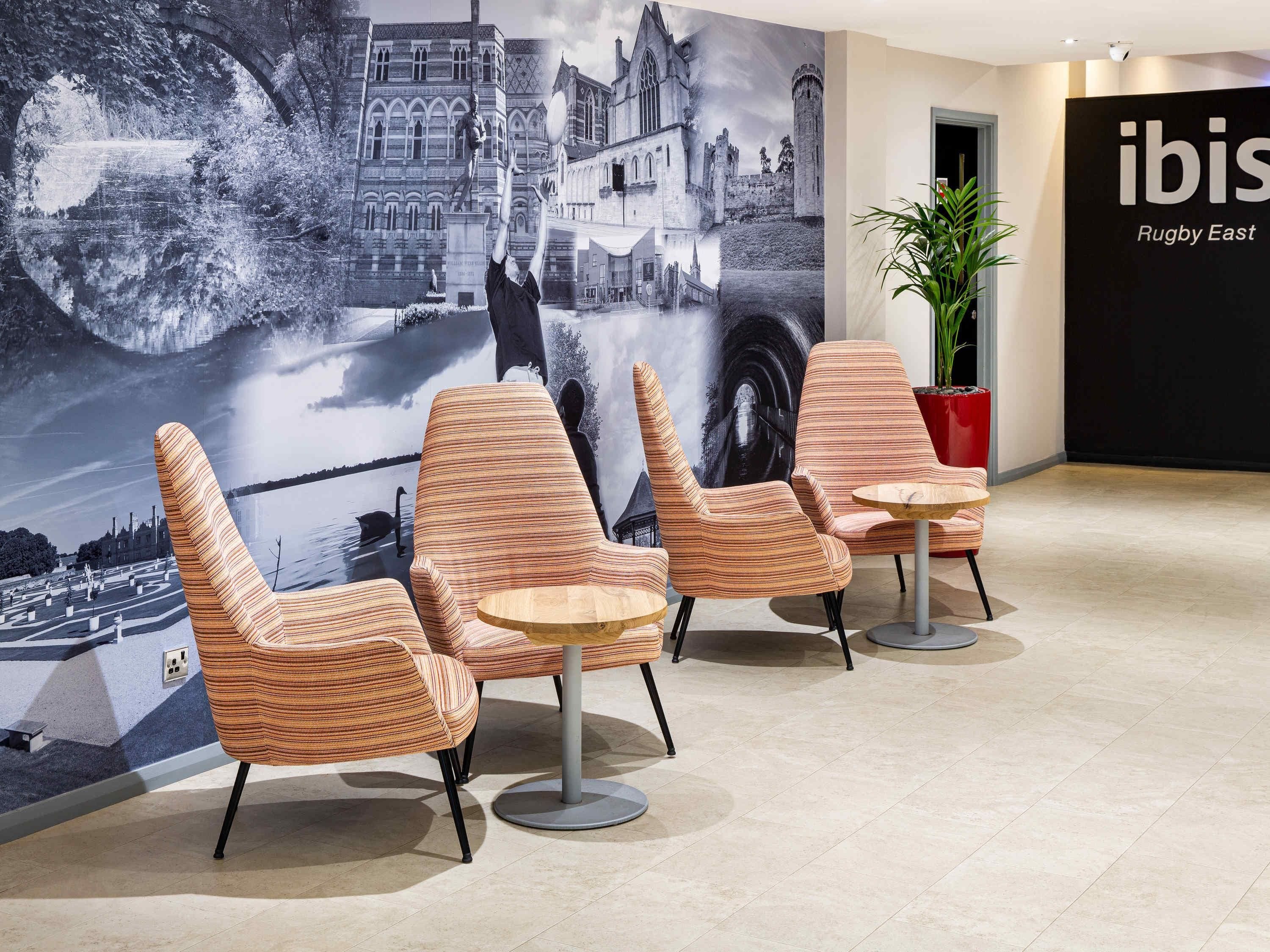 A lobby with striped chairs, a large wall mural, a plant, and a sign for 'ibis Rugby East'.