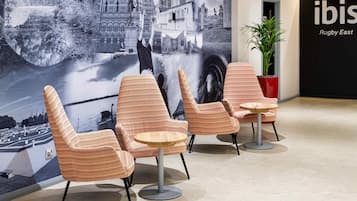 A lobby with striped chairs, a large wall mural, a plant, and a sign for 'ibis Rugby East'.