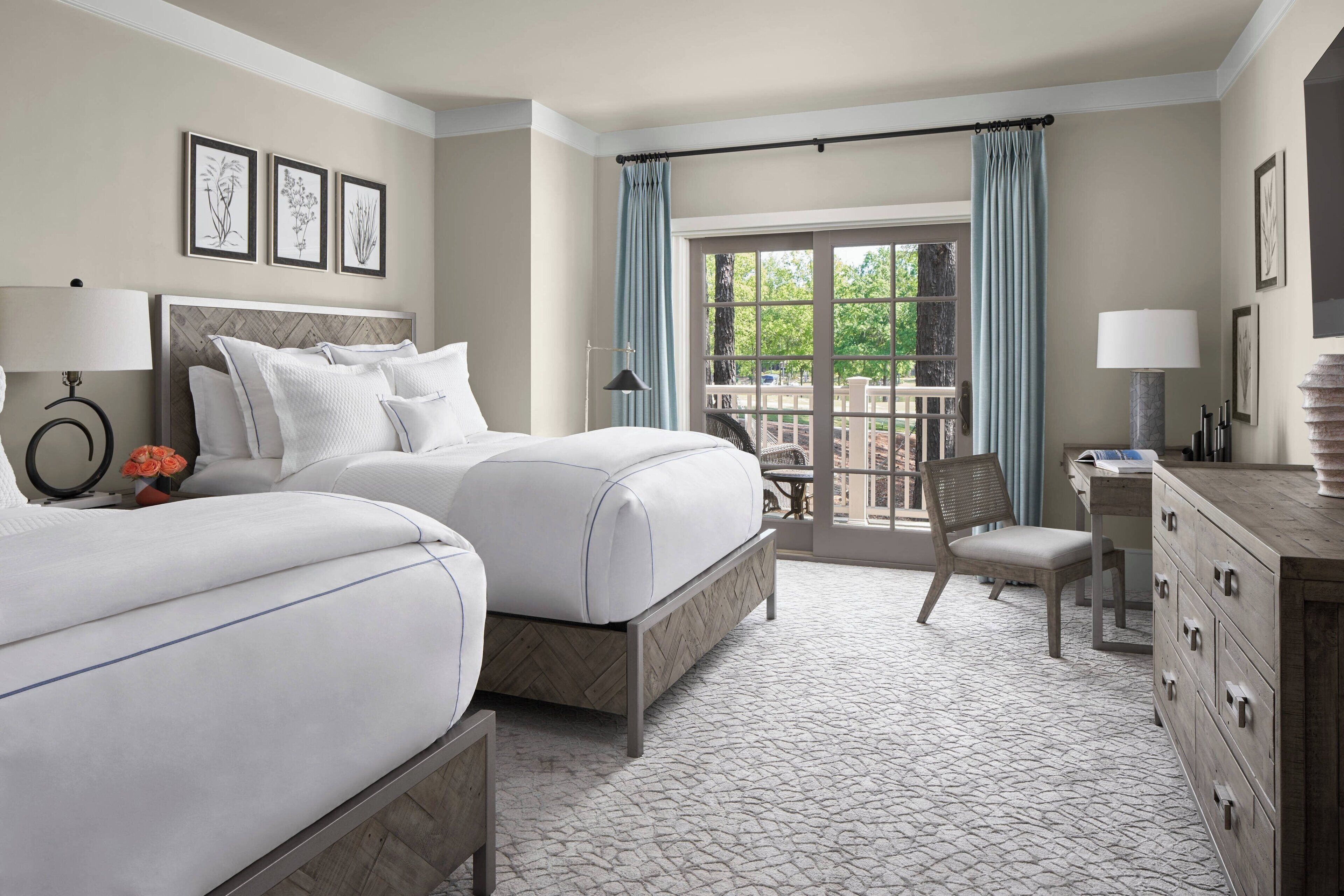 A hotel room with two beds, a desk, a chair, and a balcony with a view.