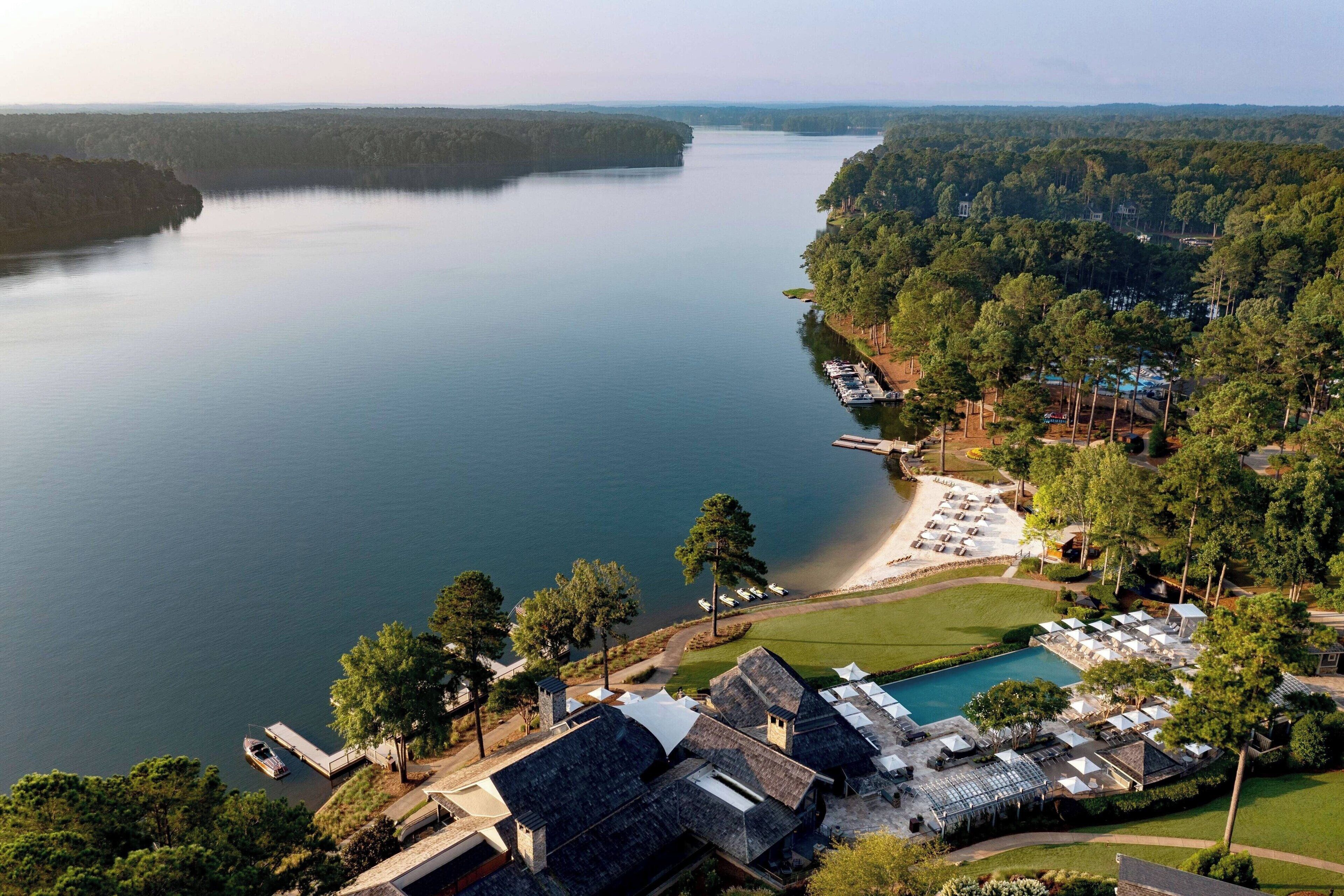 An aerial view of a lakeside resort with a swimming pool, beach, and multiple guest rooms.