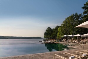 A serene pool area with lounge chairs and umbrellas, surrounded by trees and a calm lake.