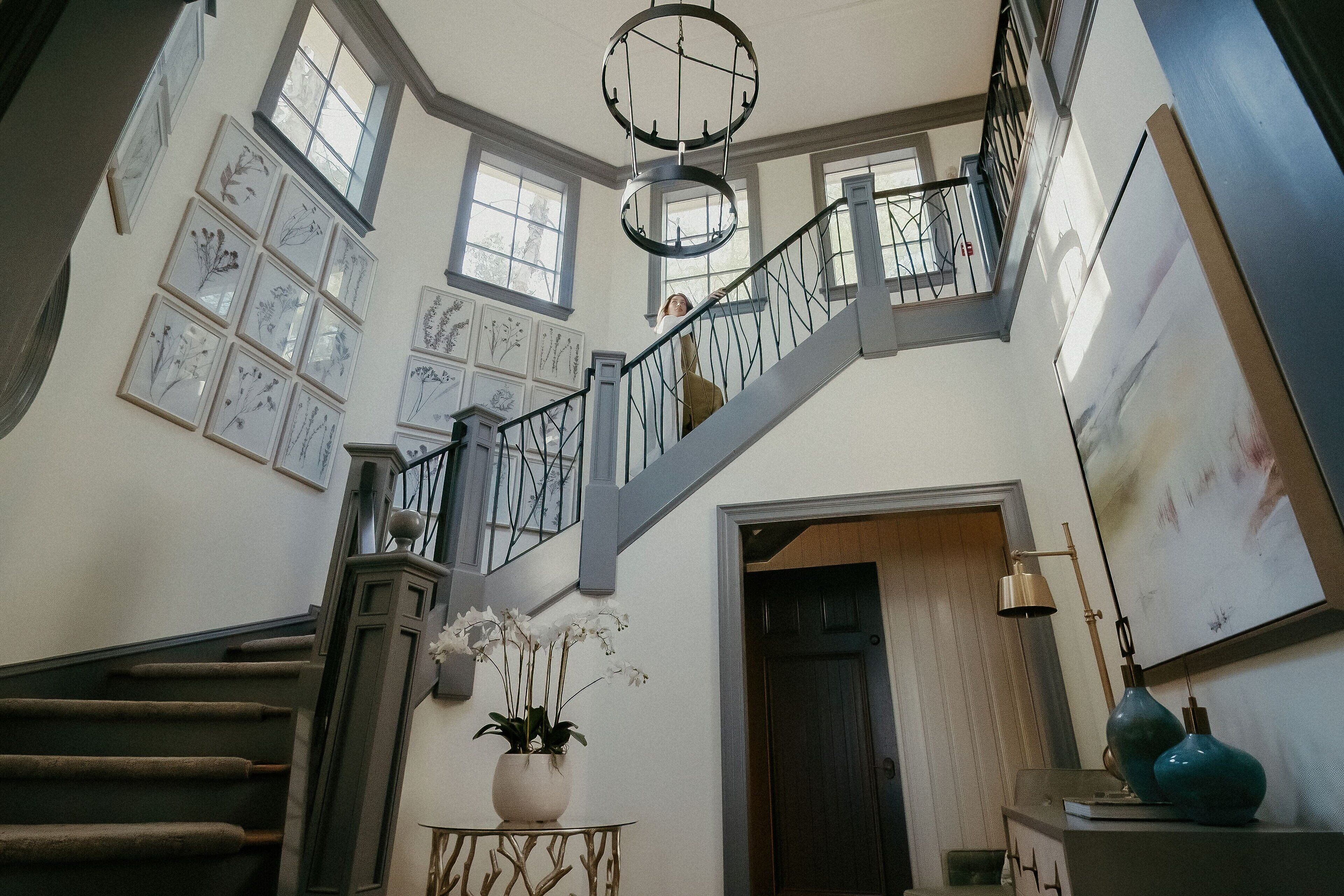 A grand staircase with a metal railing, surrounded by framed botanical prints on the walls.