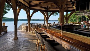 Un espace bar abrité, doté d’un sol en pierre, de chaises en bois et offrant une vue sur un lac.
