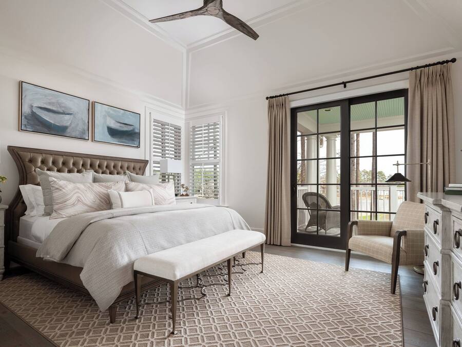 A bedroom with a large bed, a bench, a dresser, and a chair. There are two windows with shutters and a view of the outside.