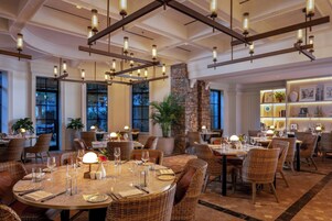 A restaurant with round tables, wicker chairs, and pendant lighting.