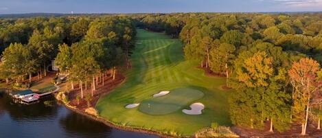 A golf course with a water body on one side, surrounded by dense trees.