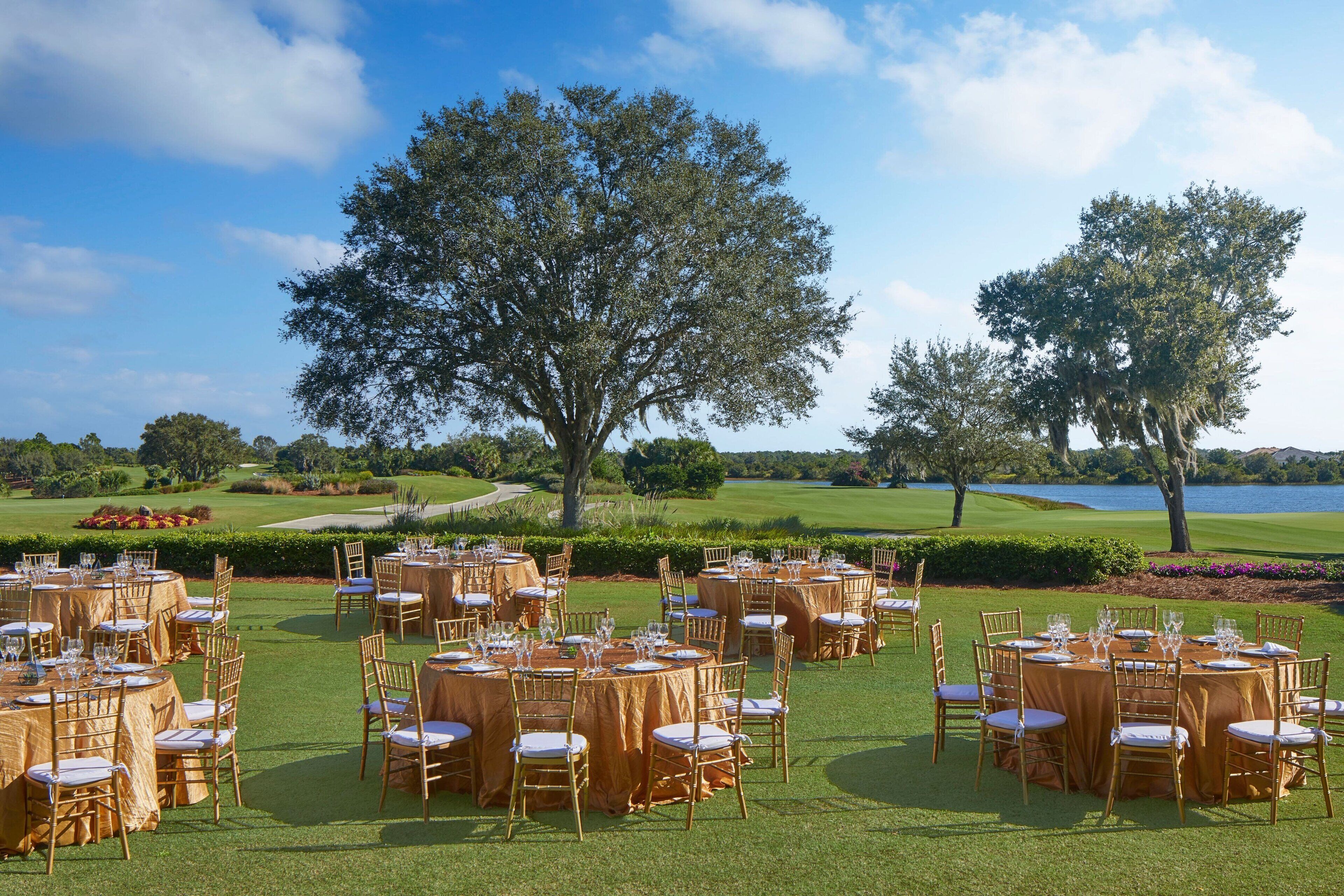 A golf course setting with round tables and chairs arranged for an event.