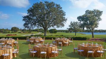 A golf course setting with round tables and chairs arranged for an event.