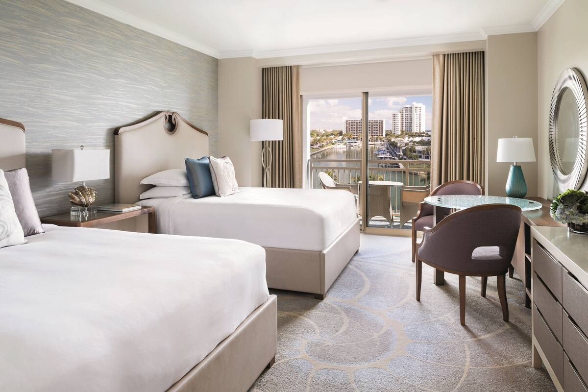 A hotel room with two beds, a dining area, and a view of a cityscape.