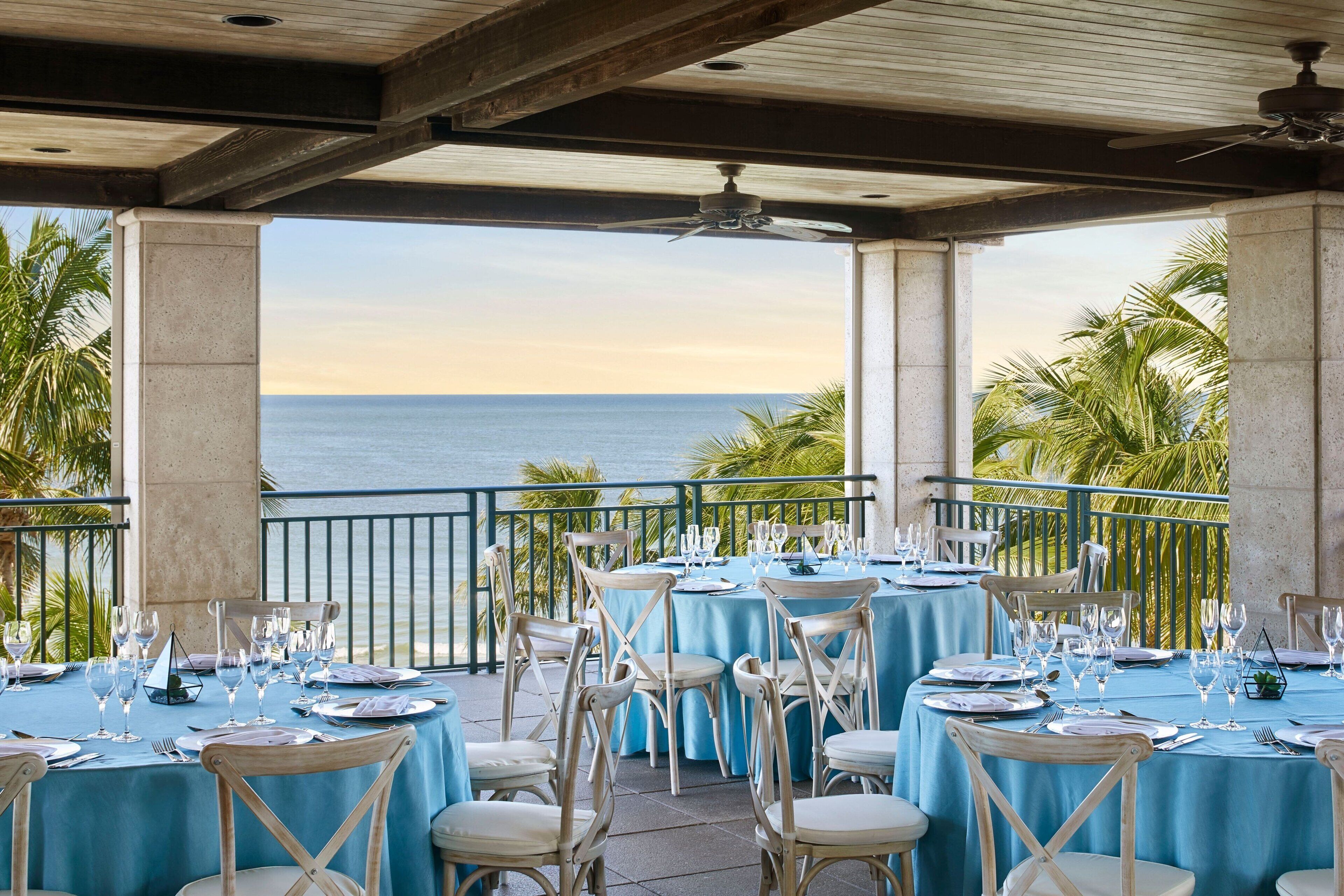 Un espace de restauration en plein air, avec des tables dressées pour le repas, offrant une vue sur l’océan.
