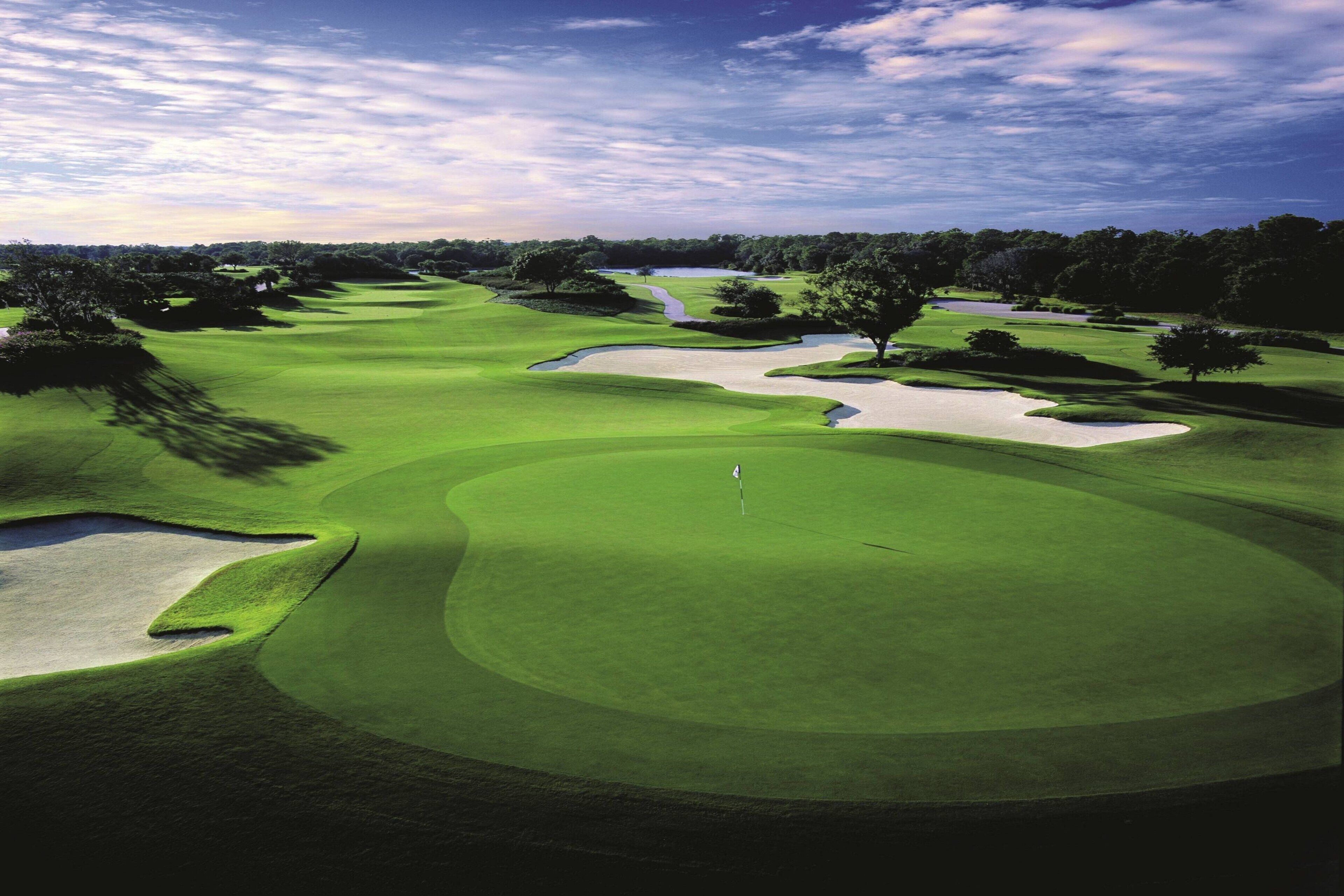 Campo de golf con búnkeres de arena, un obstáculo acuático y árboles.