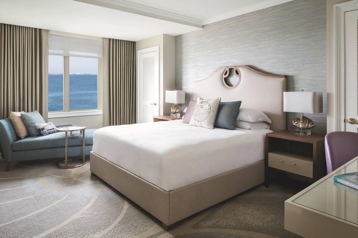 A hotel room with a large bed, a sofa, a small table, and a view of the sea.